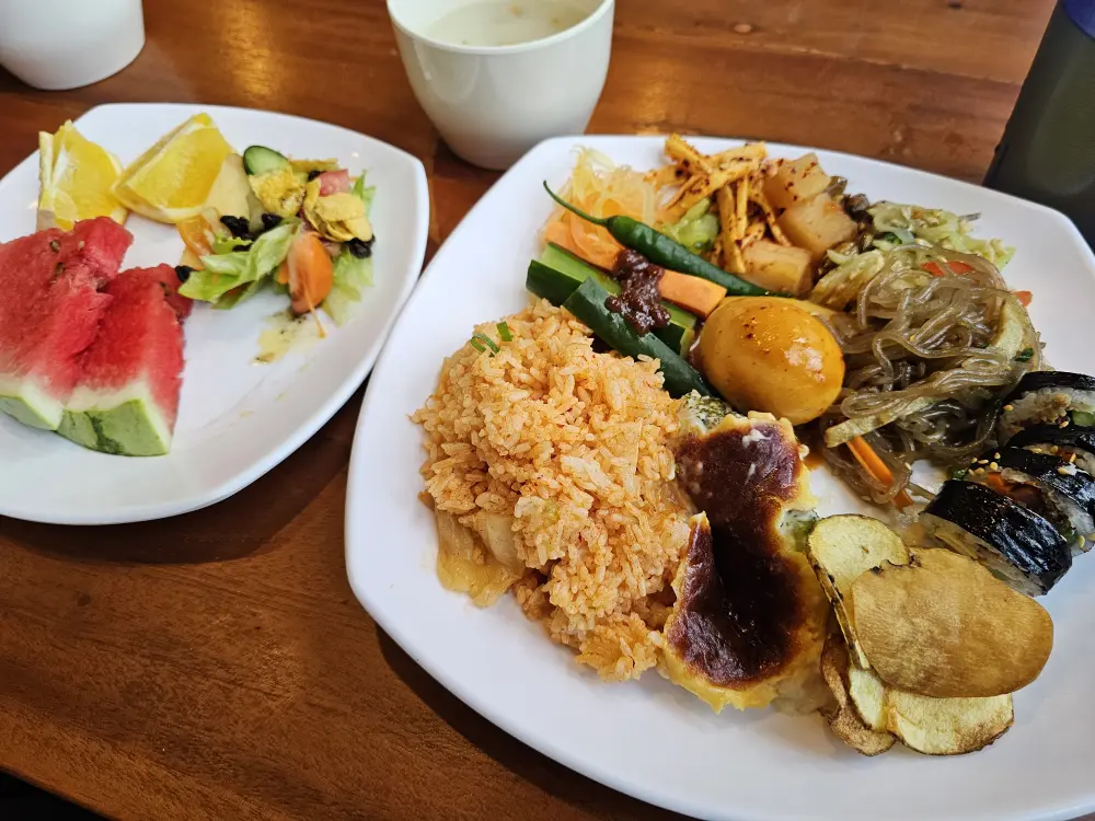 チャプチェ、キムパプ、トッポッキ、キムチチャーハン、サラダ、スイカなどが盛られた昼食