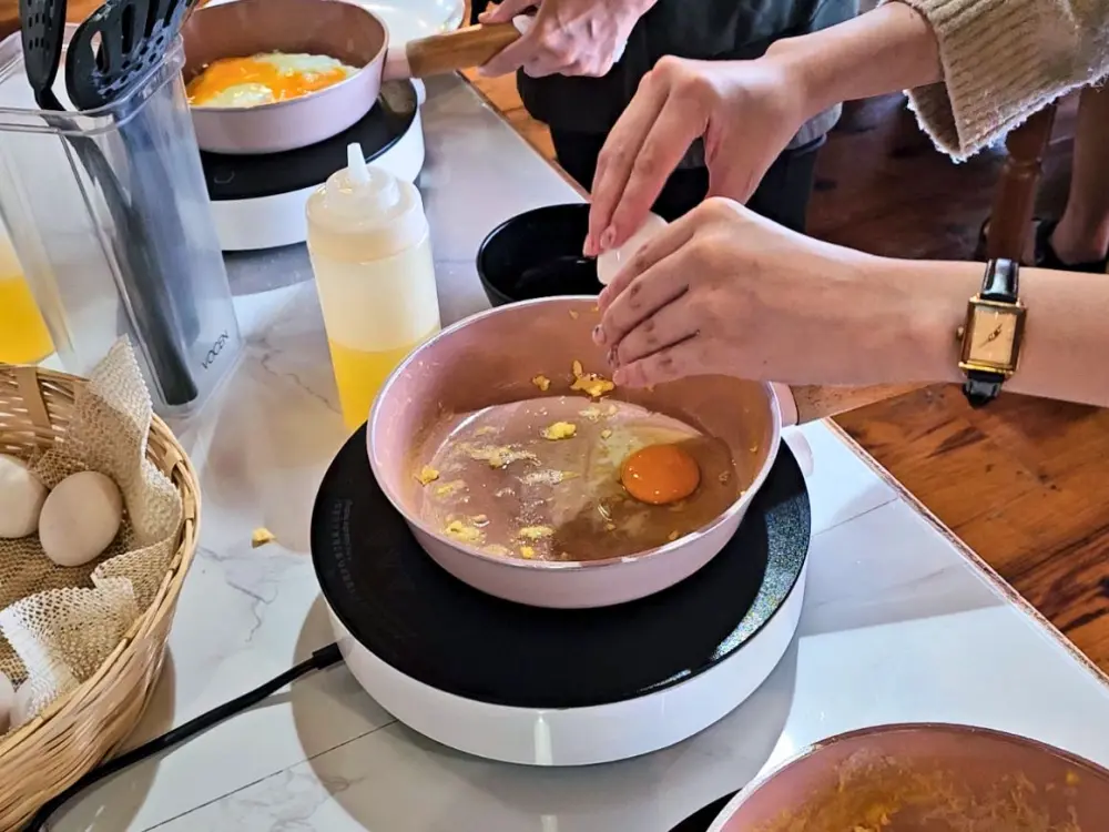 朝食カウンターに設置されたIHヒーターとフライパンで卵を調理している学生