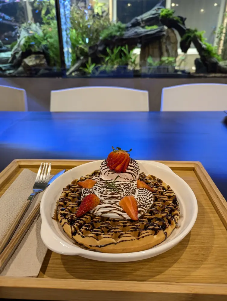 ホイップクリーム、チョコソース、苺でデコレーションされたワッフルと熱帯魚が泳ぐ水槽