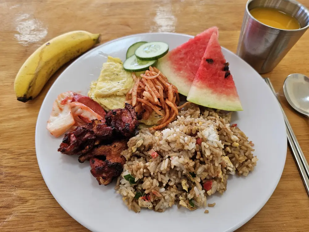 炒飯、チキン、野菜炒め、オムレツ、キュウリ、スイカ、キムチが盛られた朝食プレート