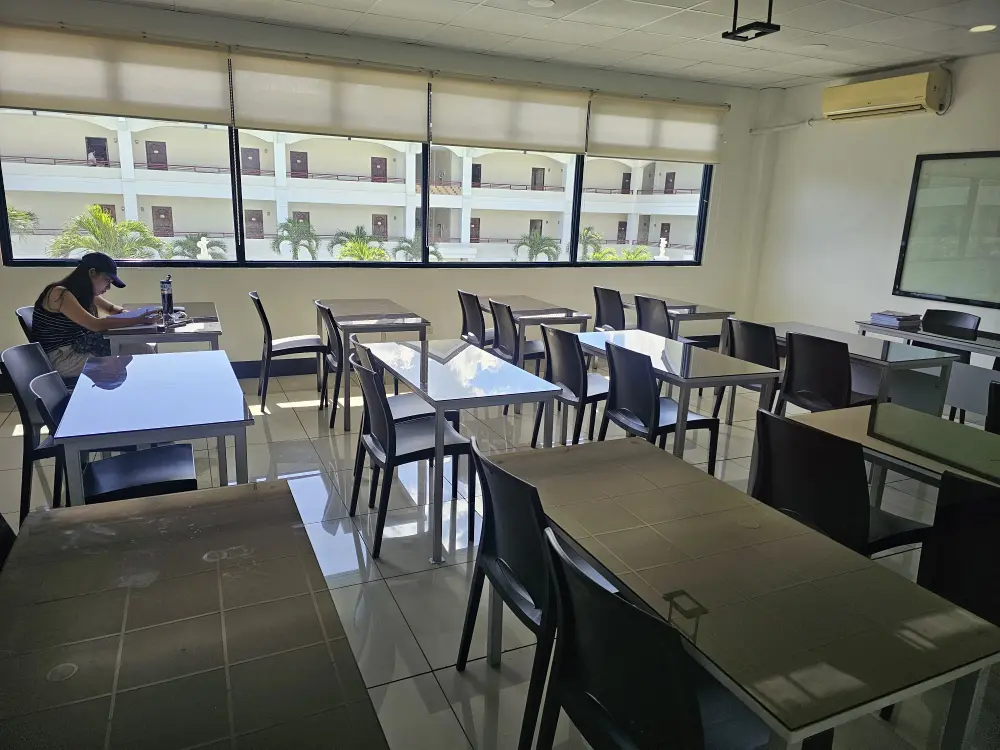 2人掛けテーブルが12台並んだCPIの自習室と窓際の席で自習する1人の学生
