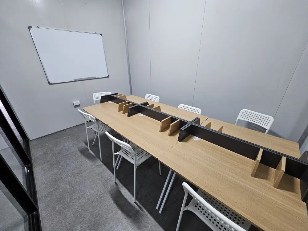 壁のホワイトボード、机6台と椅子6脚が整然と並ぶグループクラス用教室
