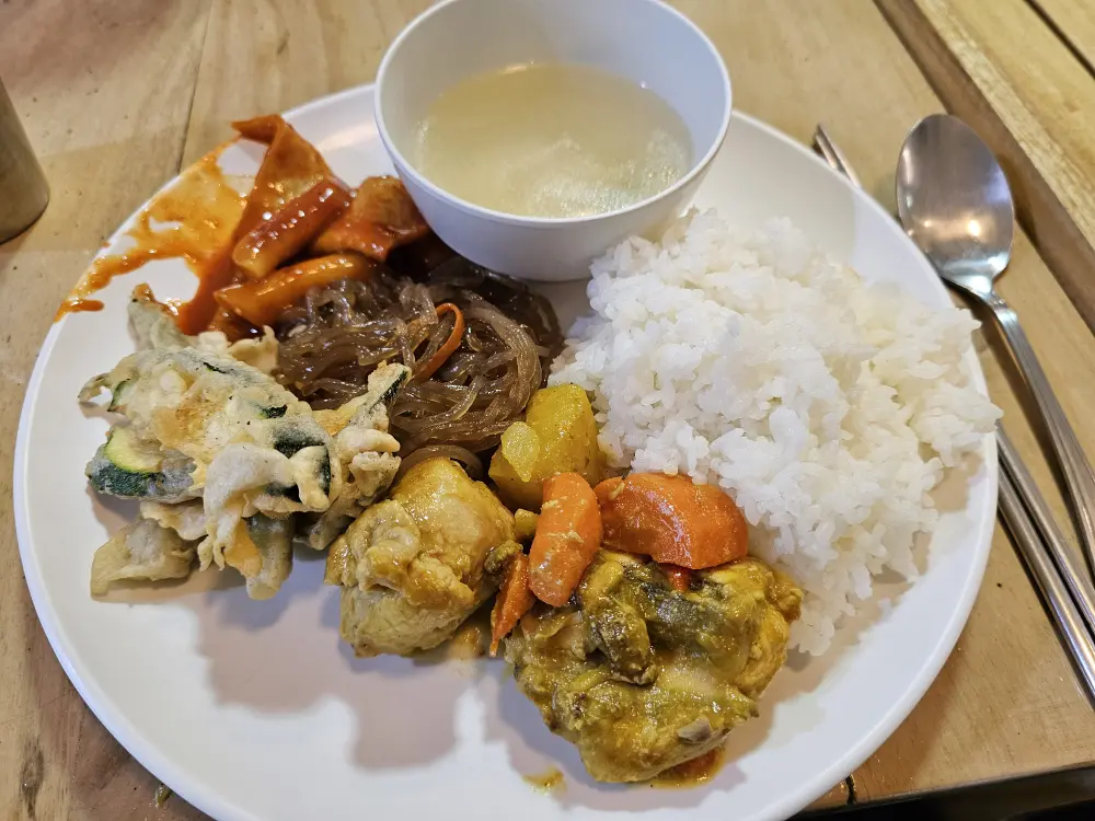 フィリピン風チキンカレー、チャプチェ、トッポッキ、ナスの天ぷらにスープが添えられたランチプレート