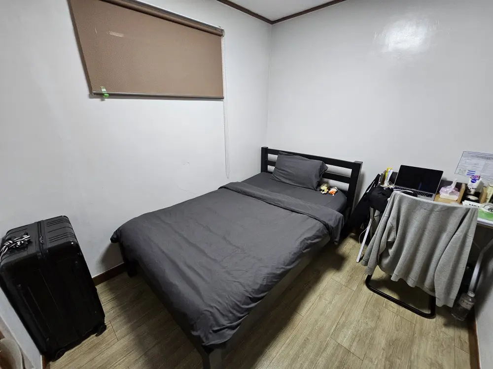 シェアタイプルームのシングルルームに配置されたシングルベッドと勉強机、学生のスーツケース