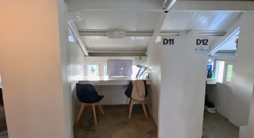 パーティションで区切られ、カウンターテーブルと2脚の椅子がある開放型マンツーマン用教室