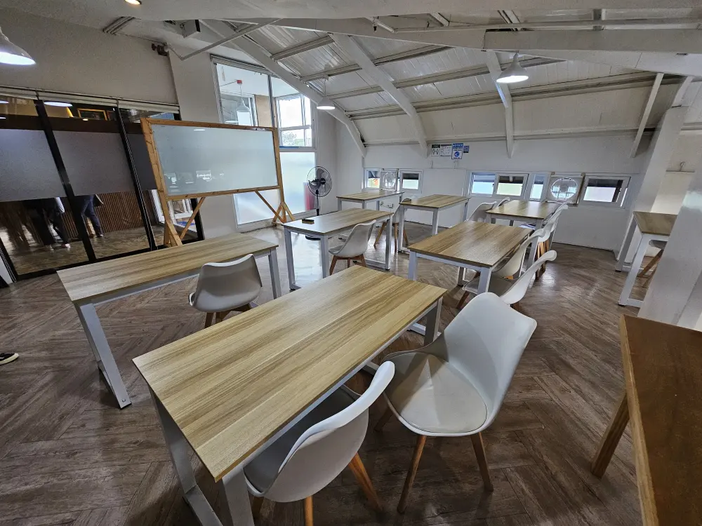 複数の窓とガラス製の壁に囲まれ、2人用テーブルと椅子が整然と並ぶプレゼンテーションルーム