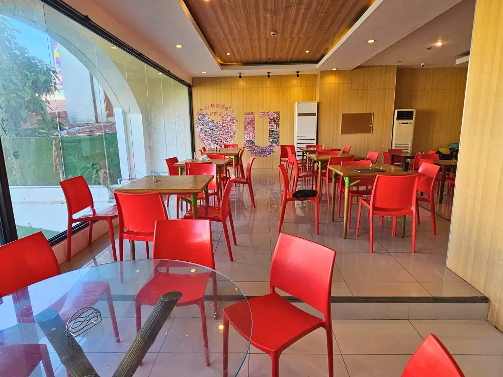 大きな窓のあるダイニングホールに整然と並べられた赤い椅子と木製テーブル