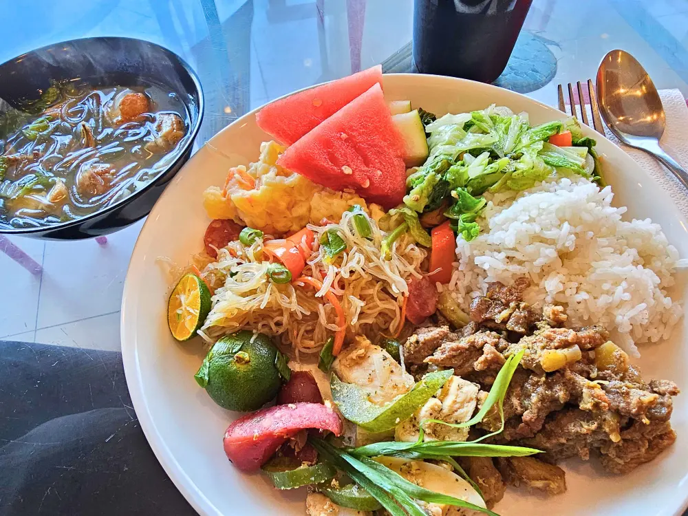 パンシット、牛肉と鶏肉料理、茹で野菜、ポテトサラダが盛られた皿にソタンホンが添えられた昼食