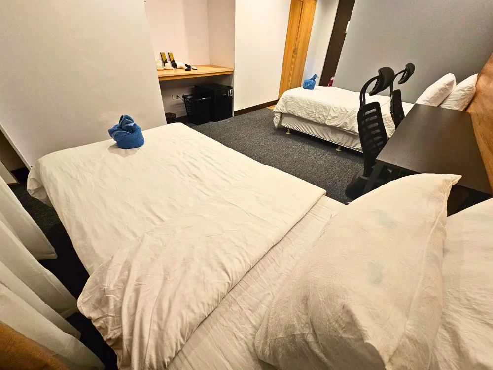 綺麗に巻かれた青いバスタオルが置かれた2台のシングルベッド、机、椅子、冷蔵庫が備わったツインルーム