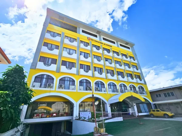 校庭から撮影した、青空の下に映えるIU English Academyの黄色と白色の校舎正面外観