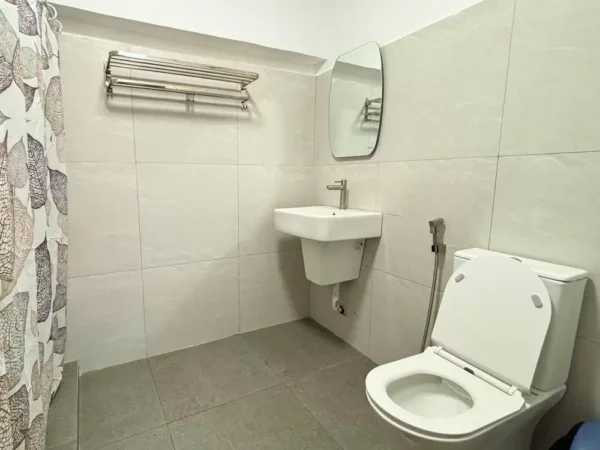 タオル掛け、洗面台、鏡、トイレが設置されたタイル張りのバスルーム