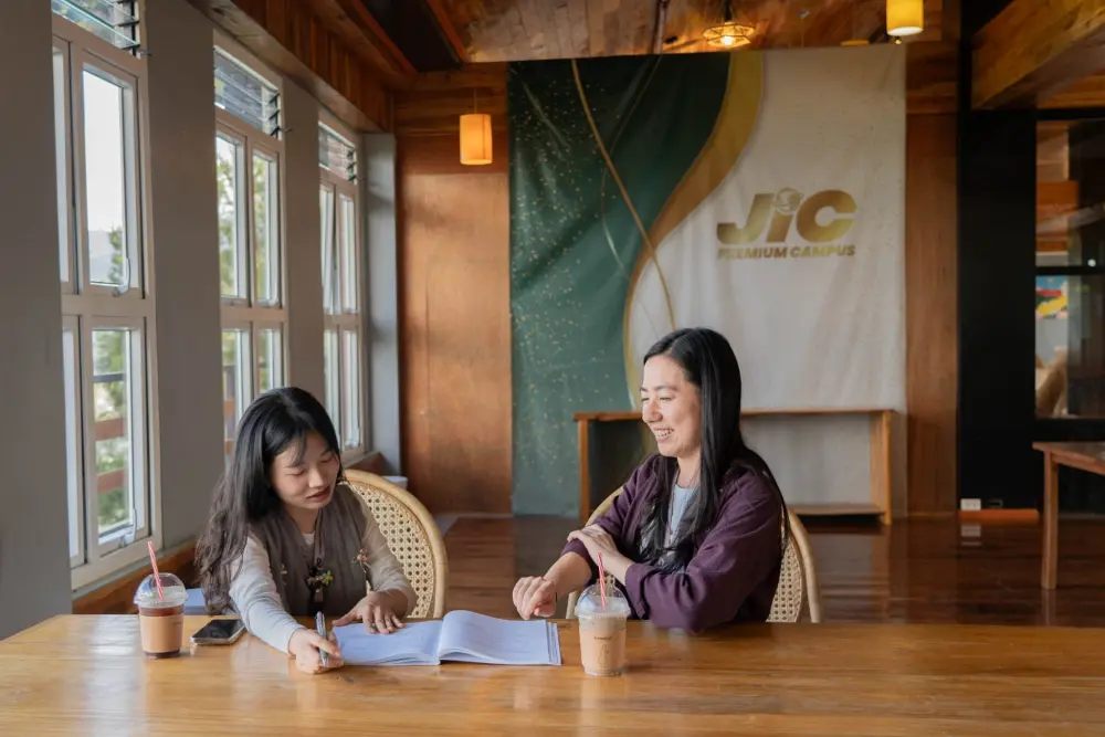 JIC Premium Campusのダイニングホールで、テーブルに座って教材を見ながら学習している2人の学生