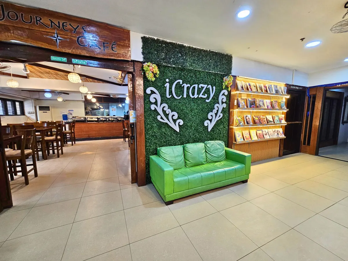 緑のソファと本棚、旧校名「iCrazy」のロゴが並ぶダイニングエリア近くのロビー