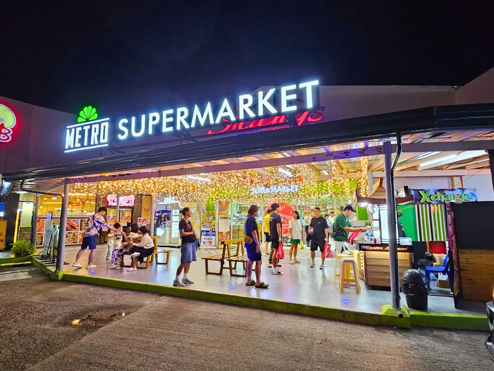 買い物客の出入りでにぎわう、夜の店頭照明が綺麗なMetro Supermarketの入口