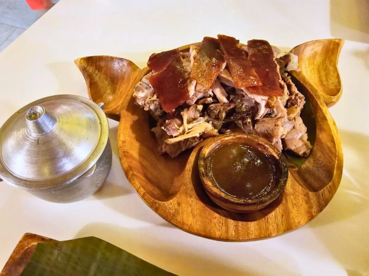 フィリピンのセブ島にあるHouse of Lechonの豚の顔をかたどった木製皿に盛られたCarcar Lechonと肉汁のソース、Plain Rice Kaldero