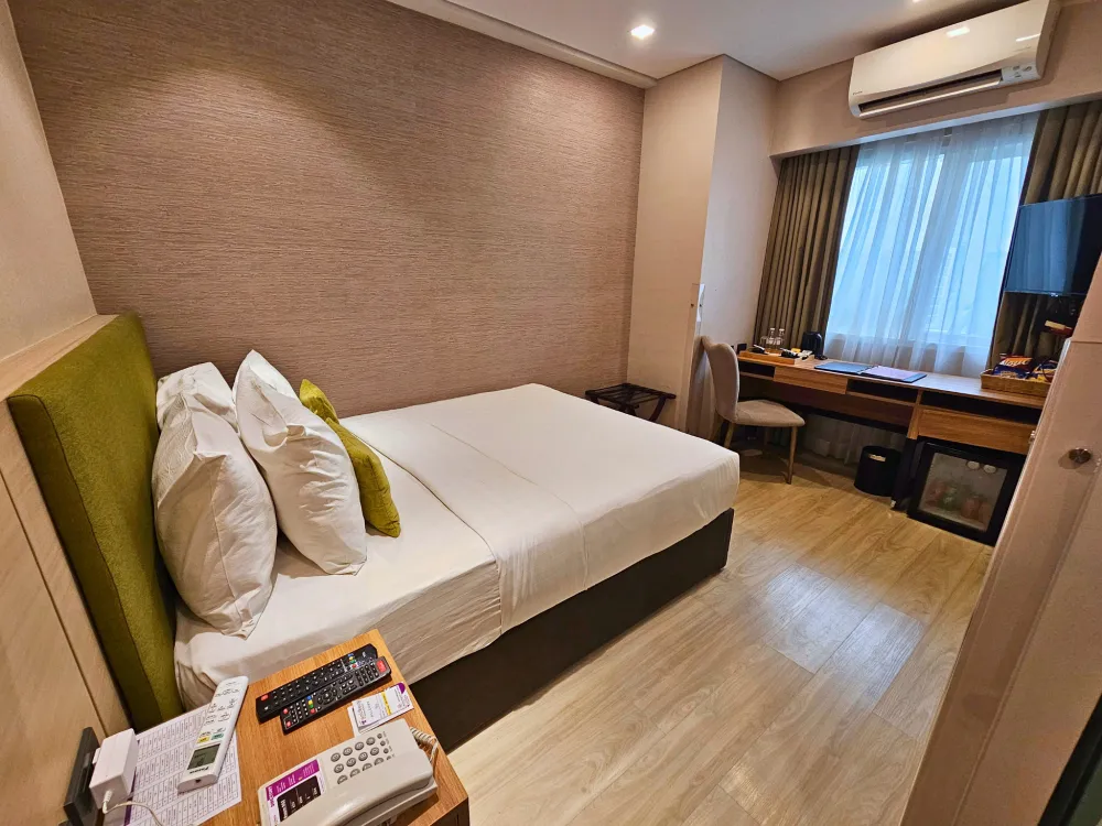クイーンベッド、ベッドサイドテーブル、エアコン、テレビ、デスクがあるGoldberry Suites & Hotel Cebuのスタジオルーム