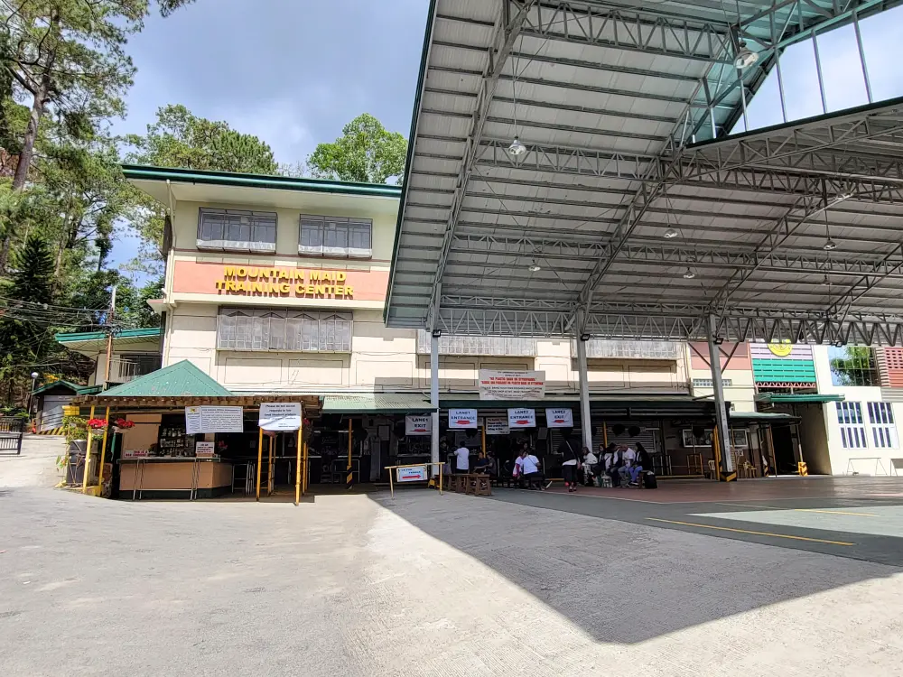屋根付きの広場と売店前で座って待つ来店客が見えるグッドシェパード修道院の建物外観
