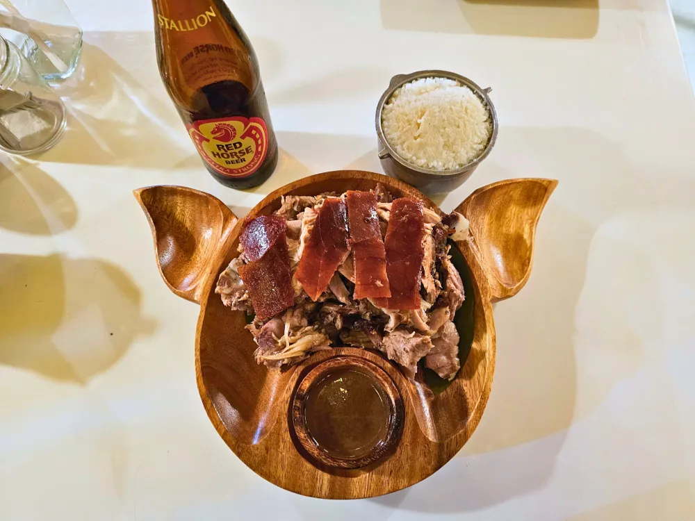 ボトル入りのレッドホースビールとPlain Rice Kaldero、豚の顔をかたどった木製皿に盛られたカルカルレチョンと肉汁のソース