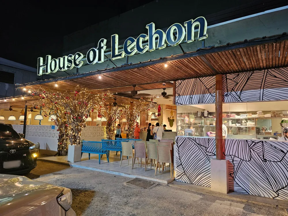 駐車場側から見たHouse of Lechonの外観と看板、ライトと赤いオーナメントで飾られた枝の装飾