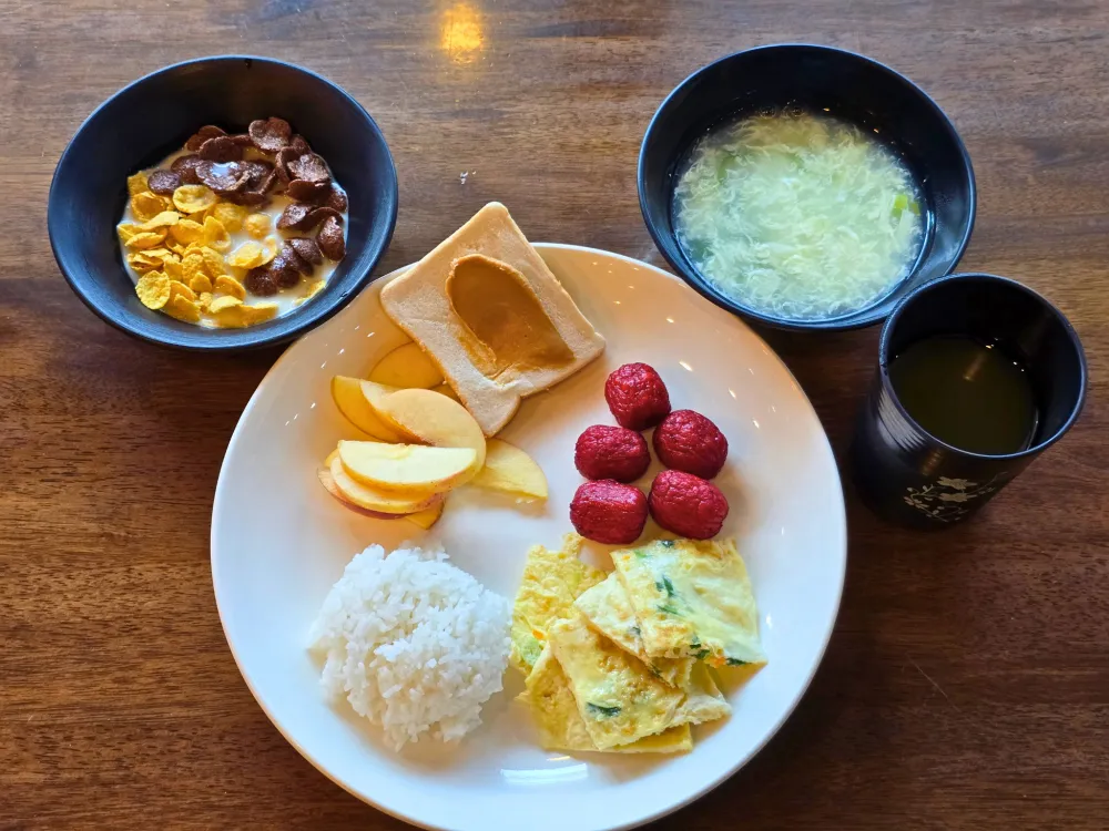 ICL English Academyの朝食に並んだ赤いホットドッグソーセージ、オムレツ、ご飯、リンゴ、食パン、シリアル、卵スープ