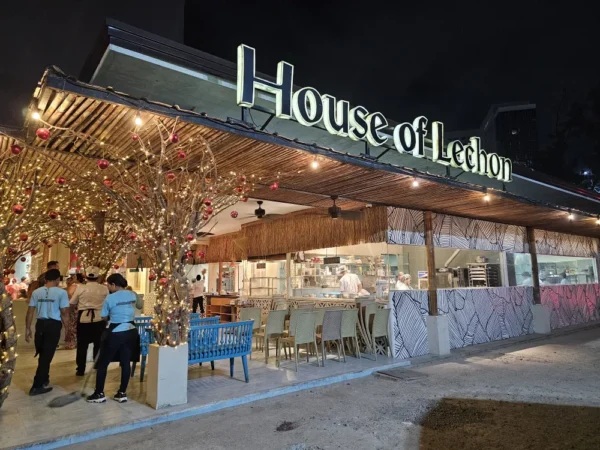 夜の駐車場側から見たHouse of Lechonの外観と看板、ライトや赤いオーナメントで飾られた枝の装飾