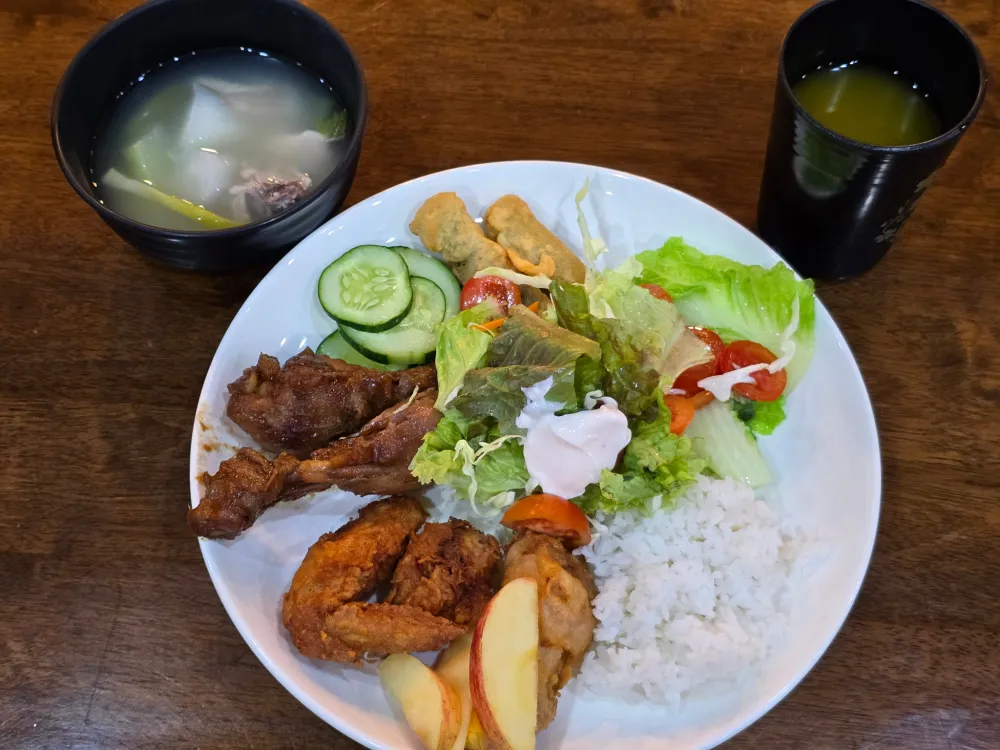 ICLの夕食に並んだチキンアドボ、フライドチキン、サラダ、ご飯、鶏肉と野菜のスープ、リンゴ、ジュース