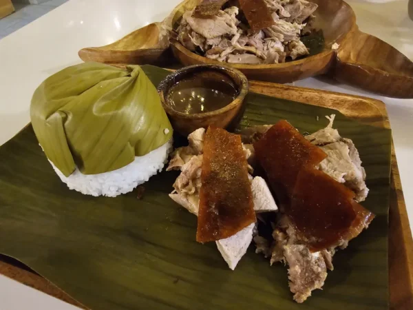 バナナリーフを敷いた皿に盛られたカルカル・レチョンの肉とパリパリの皮、バナナリーフで包まれたご飯、肉汁のソース