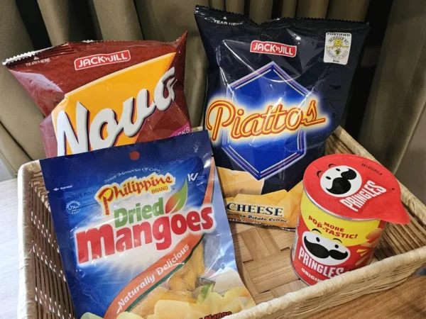 スタジオルームのデスクの上に置かれた、編みかごに入ったフィリピンのコーンチップス、ポテトチップス、ドライマンゴー、プリングルズ