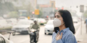 煙霧によって白く霞んだ市街地で、マスクを着用している女性のイメージ（出典：Philippine Information Agency）