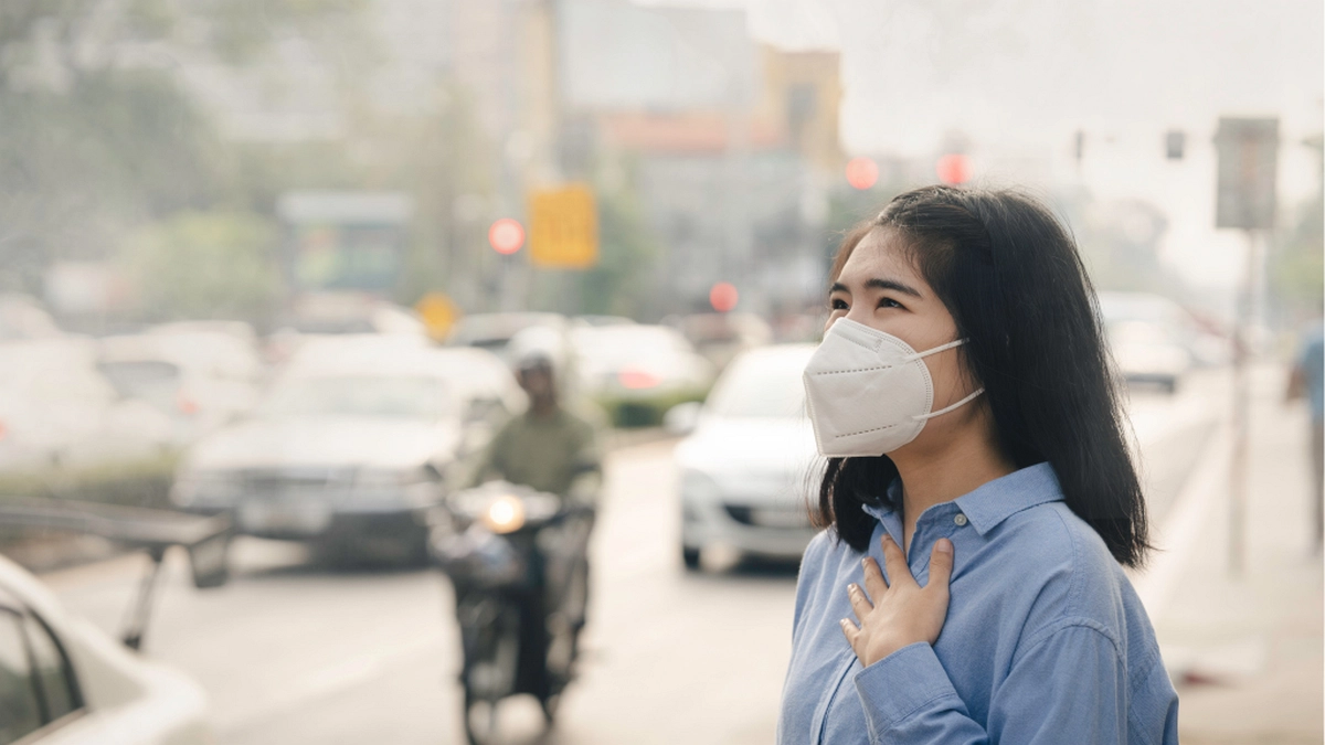 煙霧によって白く霞んだ市街地で、マスクを着用している女性のイメージ(出典:Philippine Information Agency)
