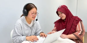 JIC Premium Campusで、ヘッドセットを着けてノートPCを操作する学生と、画面を確認する講師