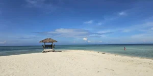 Grit留学が撮影したフィリピンのパンダノン島に広がる白砂のビーチと青い海、砂浜の先にある小屋と穏やかな海岸の風景
