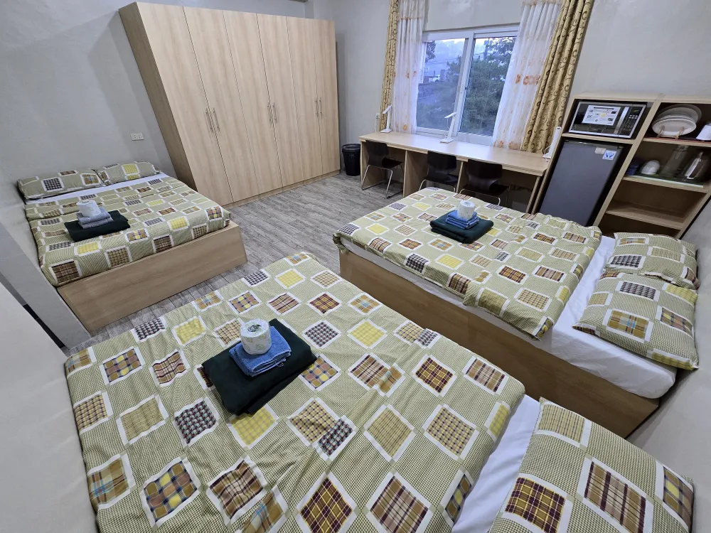 MONOL Main Campusのトリプルルーム全景、3台のベッドと大型クローゼット、窓際の3人用デスク、電子レンジや冷蔵庫などの室内設備