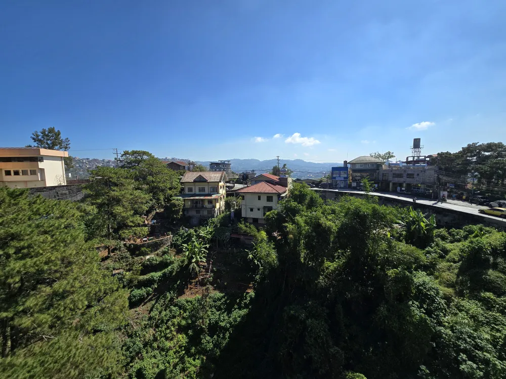 MONOL Main Campusのトリプルルームの窓から見える青空と緑豊かな住宅街、遠くに広がる山並み