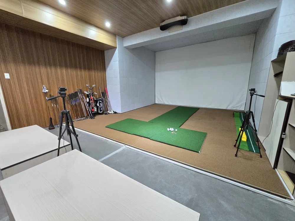 MONOL Main Campusのゴルフシミュレーター室、投影スクリーンと2台の三脚スタンド、打席マット、ゴルフボール