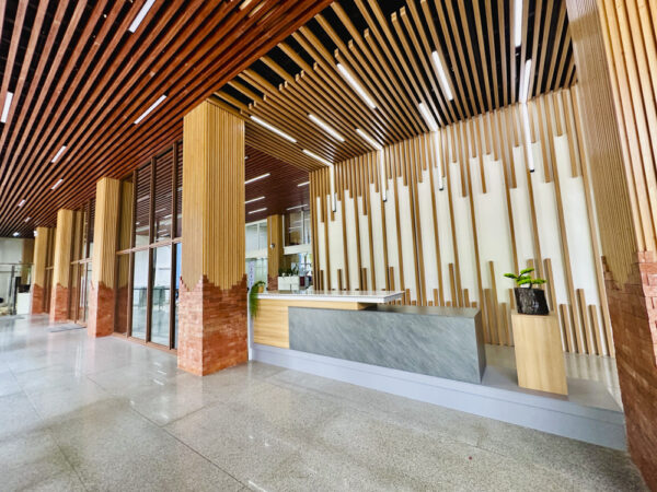 木製ルーバーで装飾された天井と壁面、受付カウンターがあるPines International Academyの校舎1階ロビー