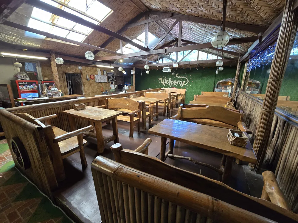 MONOLメインの校舎目の前にあるローカル食堂、Felomina’s Restaurantの店内に並ぶ木製のテーブルとベンチ、カウンター、壁面の大きな鏡