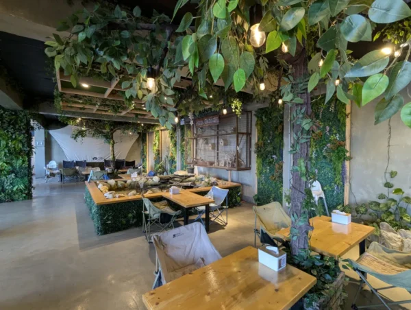 MONOL Main CampusのAqua Garden Café、緑に囲まれた店内に並ぶ木製テーブルと椅子、魚が泳ぐ四角い池