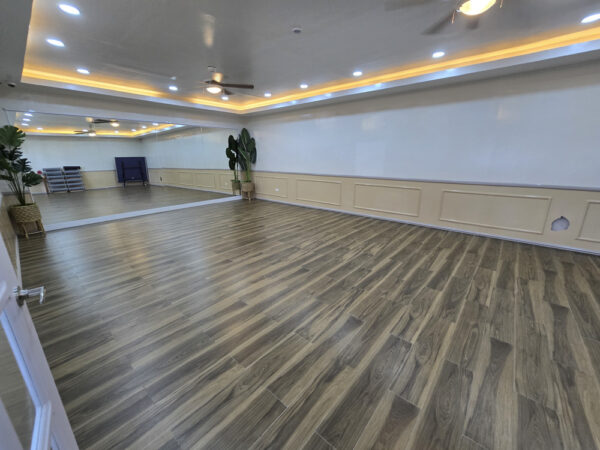 壁一面に大型の鏡が設置され、奥にヨガマットと折りたたんだ卓球台が置かれたヨガスタジオ
