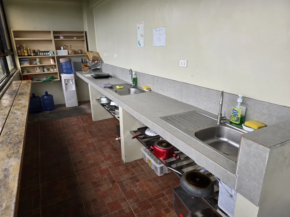 MONOL Main Campusの共用キッチン、2つのシンクと電気コンロ、調理用の鍋、ウォーターサーバー、調味料を置いた棚