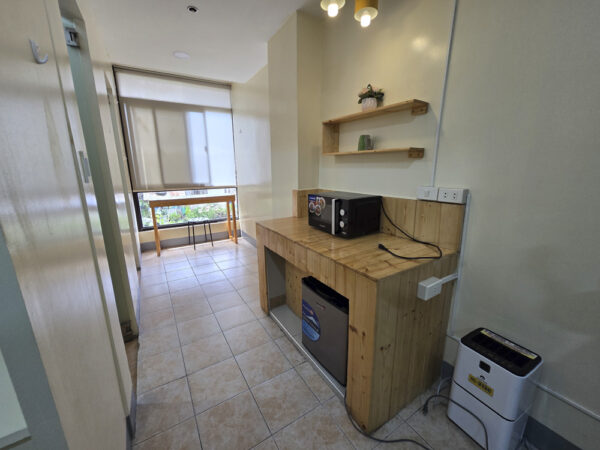 電子レンジと冷蔵庫を備えた木製カウンター、除湿機、窓際のテーブルがある1人部屋A