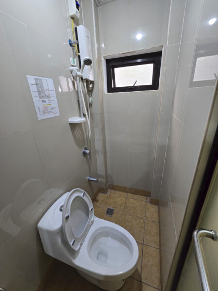 電気式シャワーヒーターとハンドシャワー、トイレが同じ空間に設置された1人部屋Ｂのバスルーム