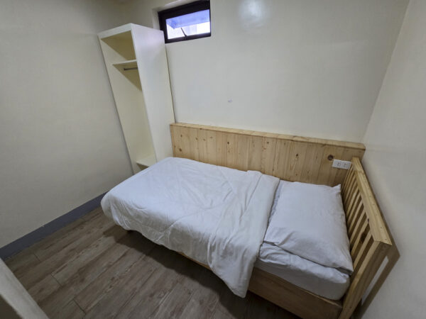 入口から見た、木製ベッドとオープンクローゼット、壁上部に小窓がある1人部屋Ｃ