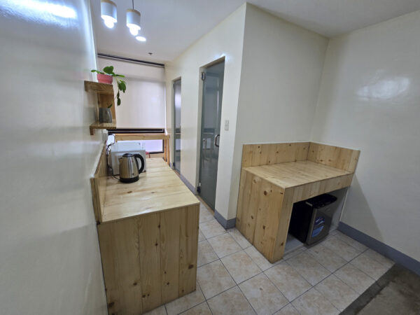 電子レンジと電気ケトルを置いた木製カウンター、冷蔵庫、1人部屋Ｃのバスルームがある共用エリア