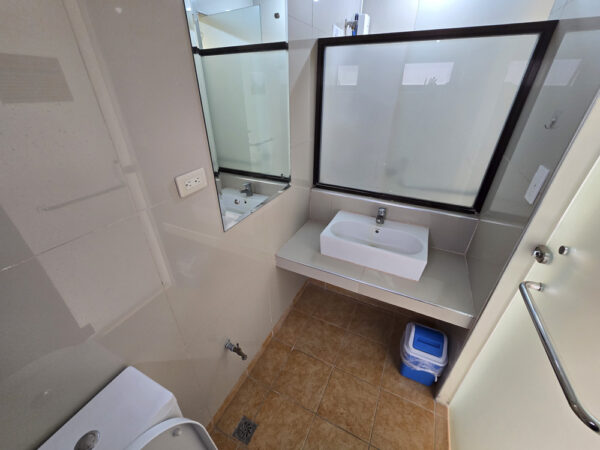 壁掛け鏡と洗面台、ゴミ箱が設置された2人部屋Ａのトイレ内の洗面スペース