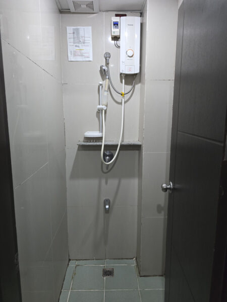 電気式温水シャワーと小物置きが設置された4人部屋Type2の独立したシャワールーム