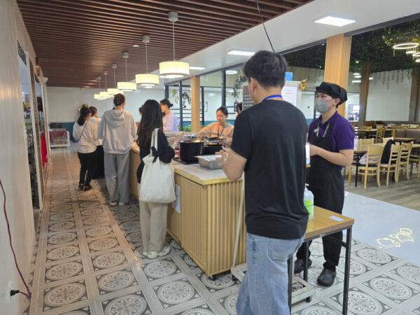 昼食時にビュッフェカウンターで料理を取り分ける学生たちとキッチンスタッフ