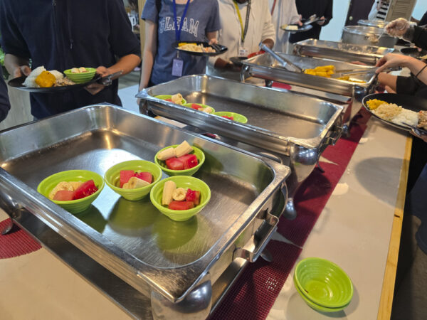 スイカとバナナが小分けに盛り付けられた緑色の器が並ぶ昼食時のビュッフェカウンター