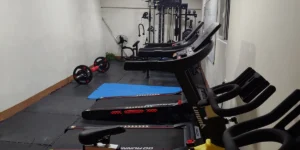 フィリピンのバギオにあるMONOL Sparta Campusの校内ジム全景。細長い室内にトレッドミルと黄色いスピンバイクが並び、奥には筋力トレーニング用のマルチジム、左側にはバーベルや青いエクササイズマットが配置されている