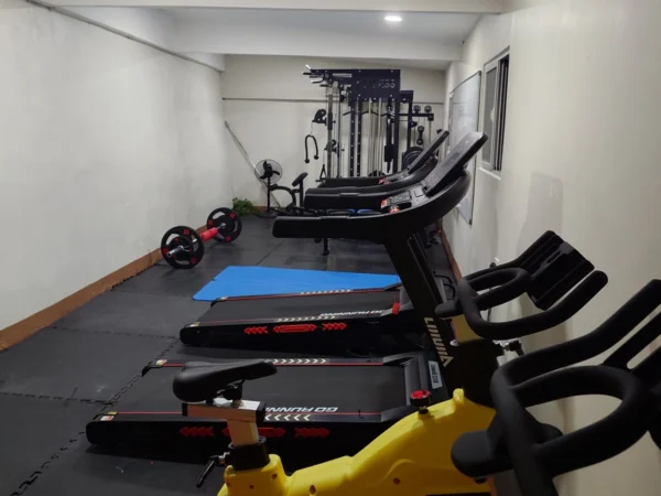 フィリピンのバギオにあるMONOL Sparta Campusの校内ジム全景。細長い室内にトレッドミルと黄色いスピンバイクが並び、奥には筋力トレーニング用のマルチジム、左側にはバーベルや青いエクササイズマットが配置されている